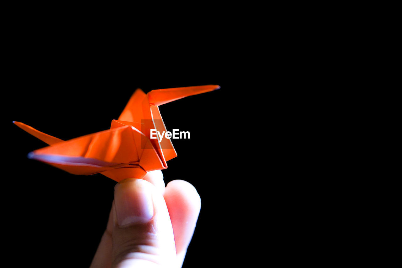 Cropped finger of person holding paper crane against black background