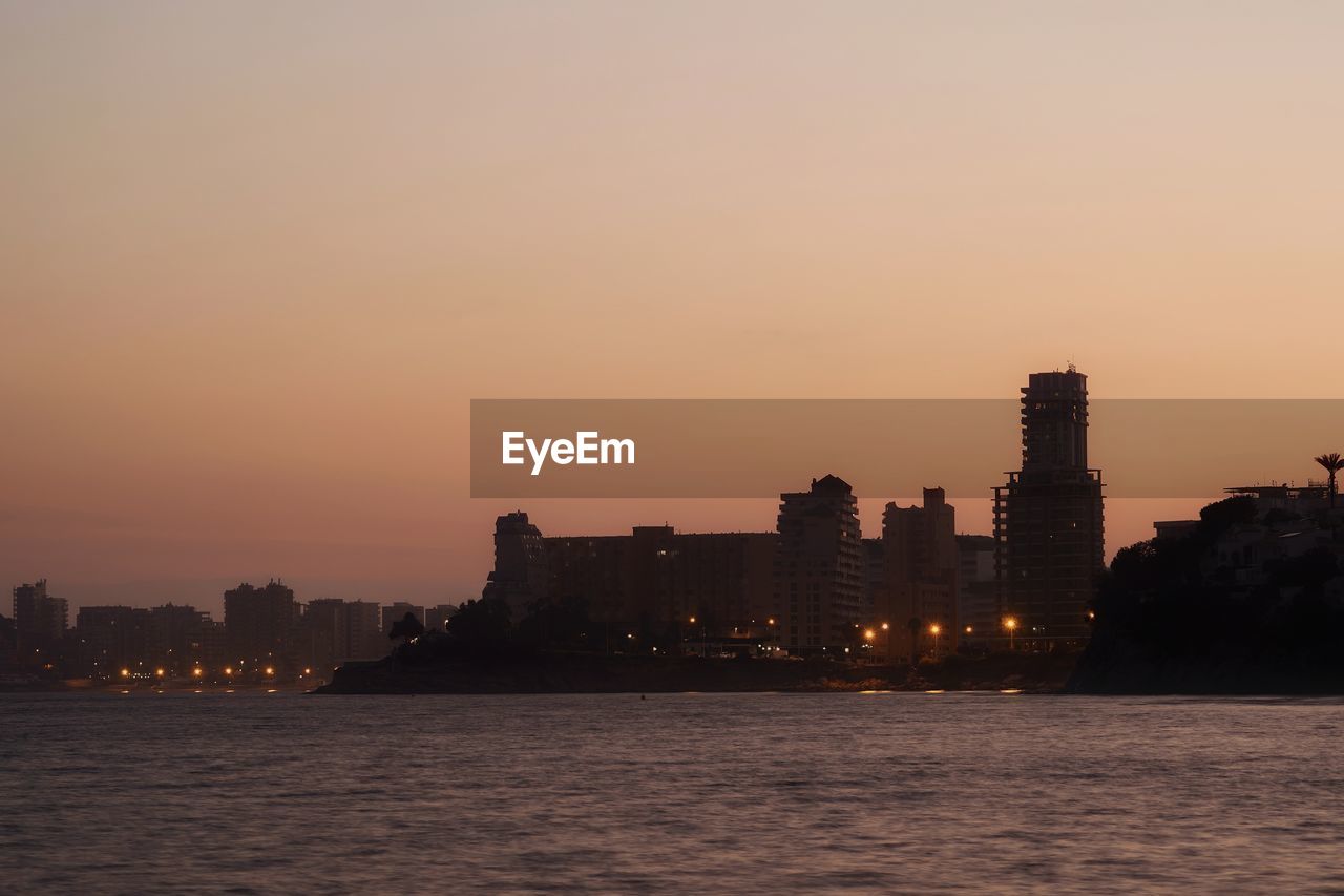 Sea by buildings against sky during sunset