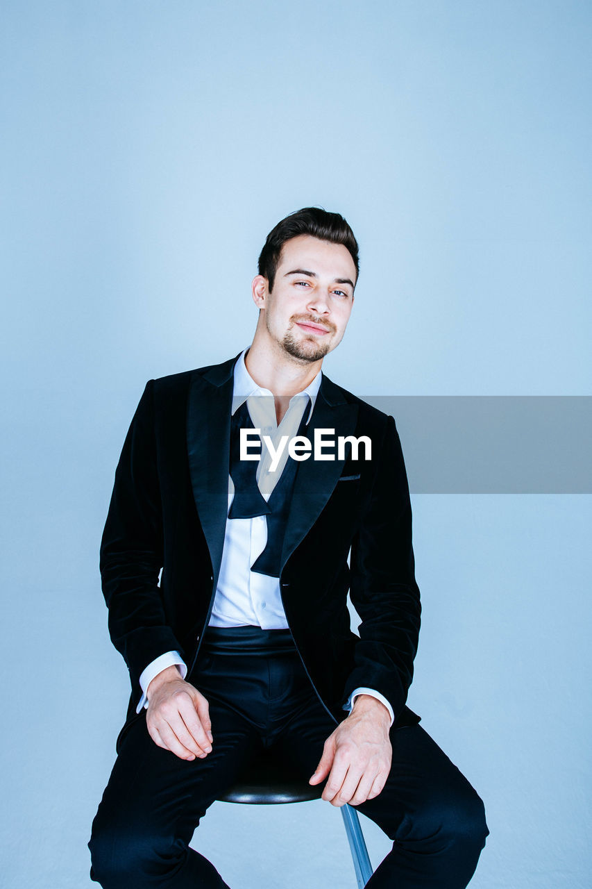 Portrait of businessman sitting on stool against blue background