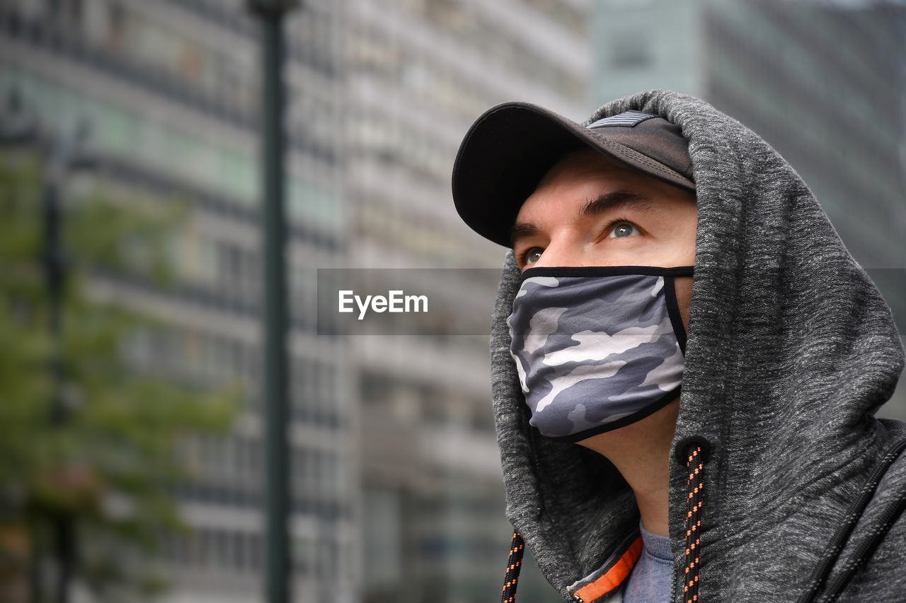 Close-up of man wearing flu mask looking away while standing outdoors