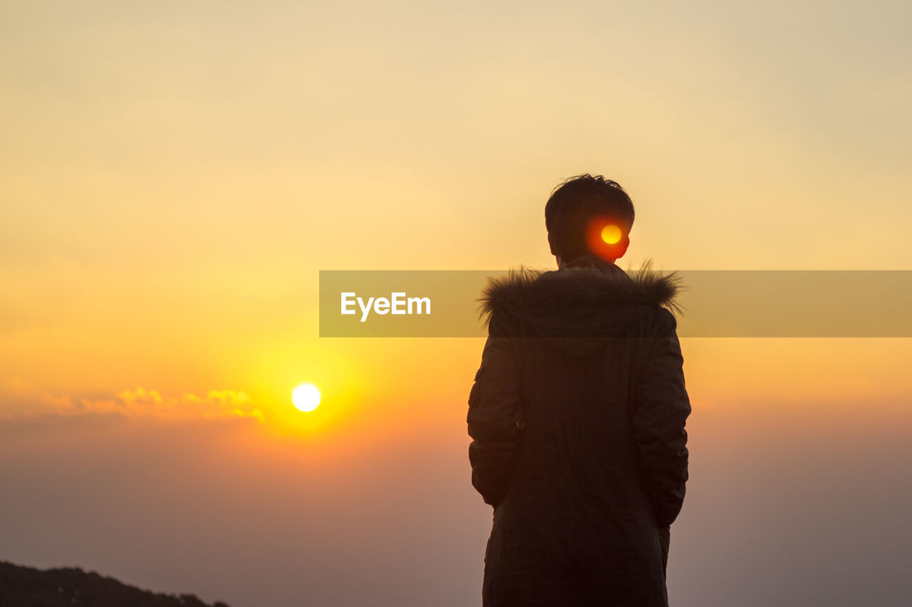 Rear view of man standing against sky during sunrise