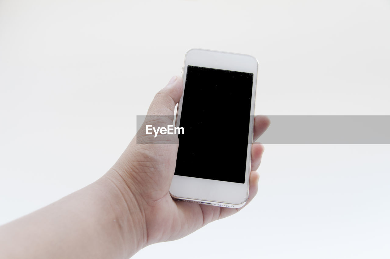 Cropped image of hand holding smart phone against white background