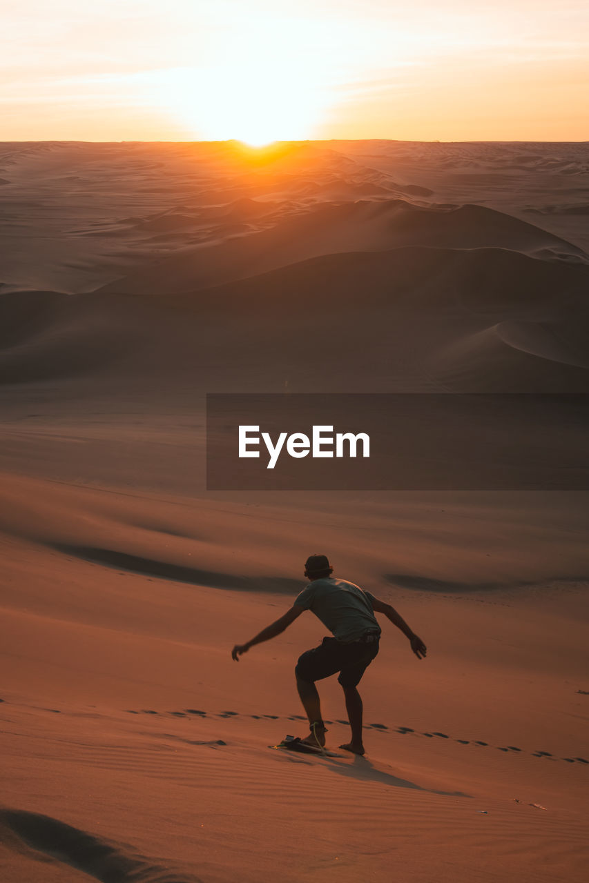 Rear view of man sandboarding at desert