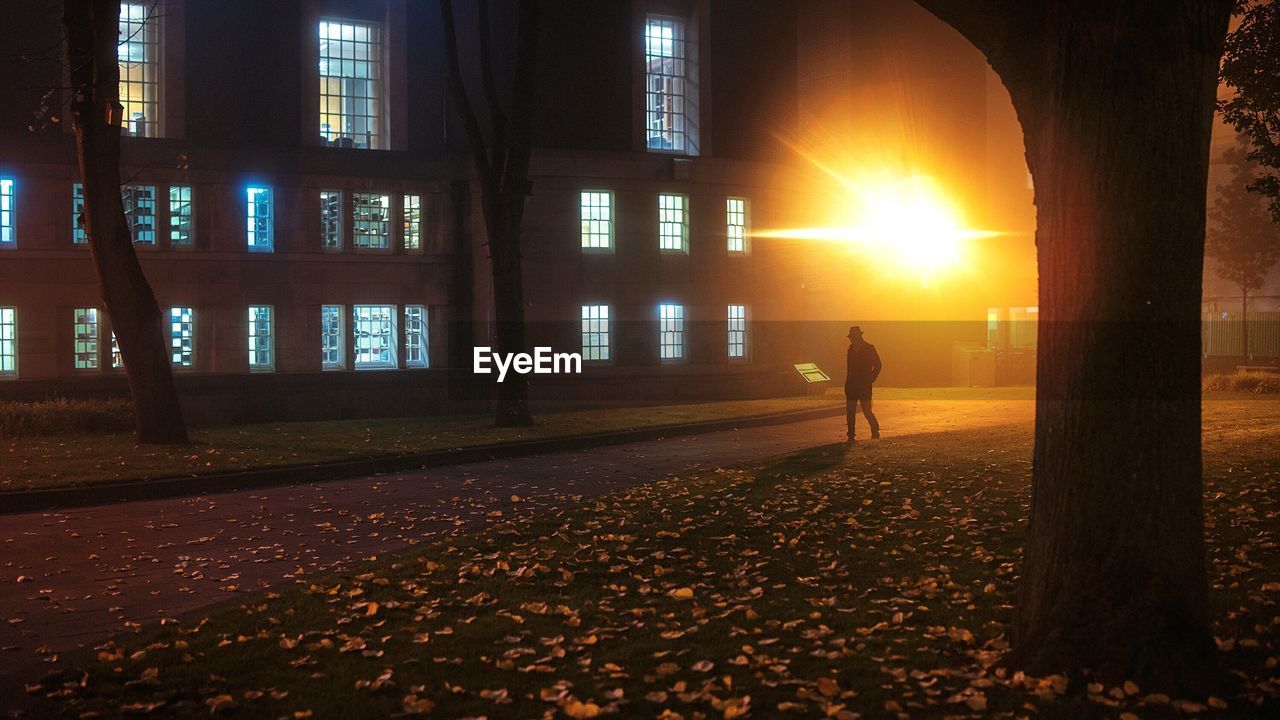 Man walking on footpath against illuminated yellow light on building