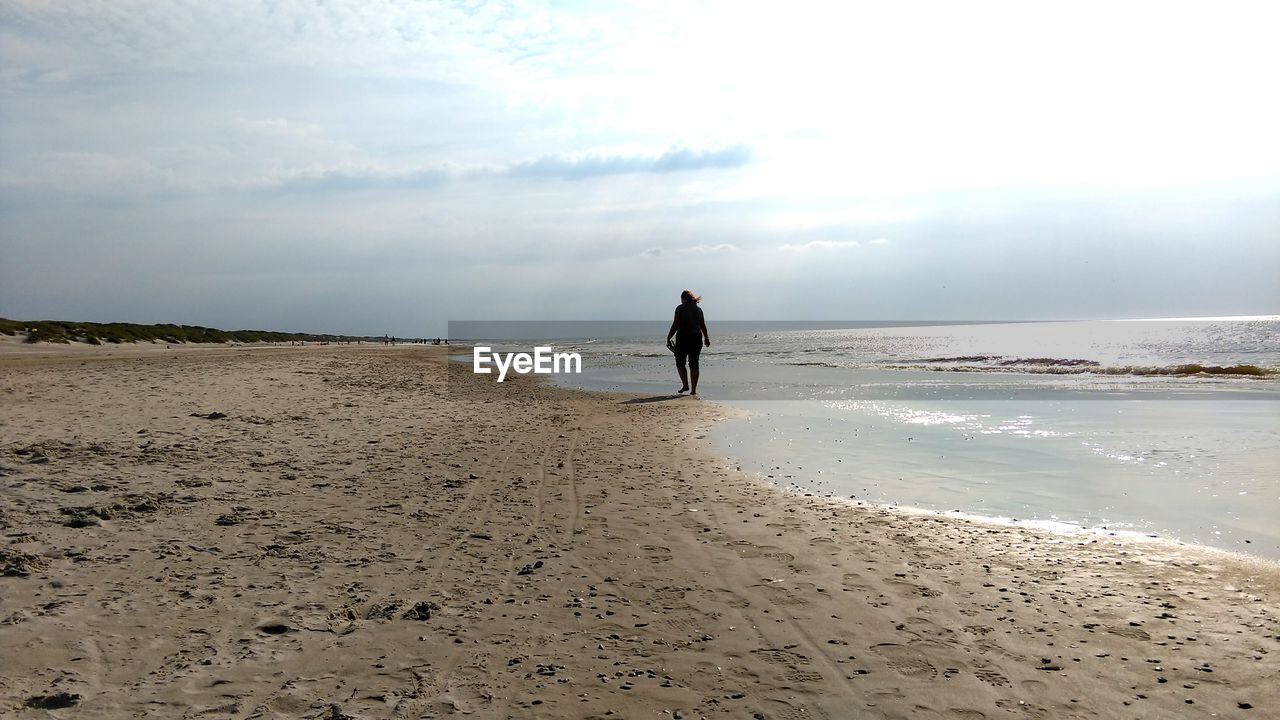 Rear view of woman walking on shore at beach against sky