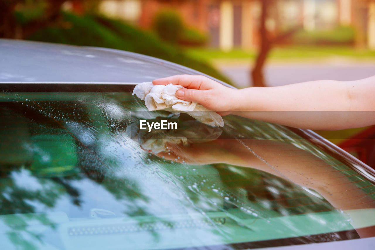 Cropped hand of woman cleaning car windshield