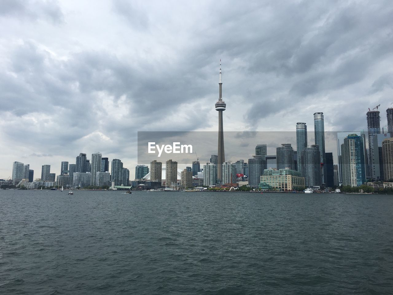 Cn tower by river against cloudy sky in city