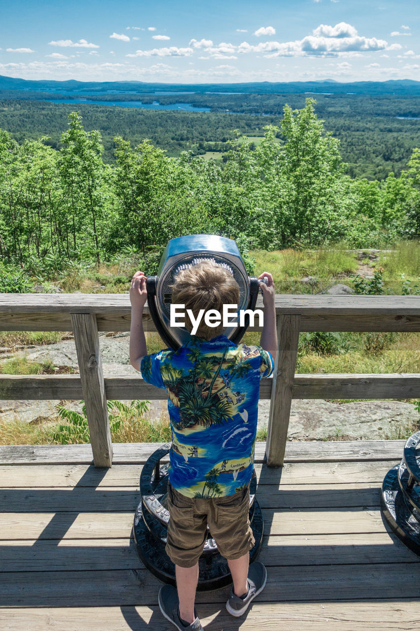 Rear view of boy looking through coin-operated binoculars at observation point