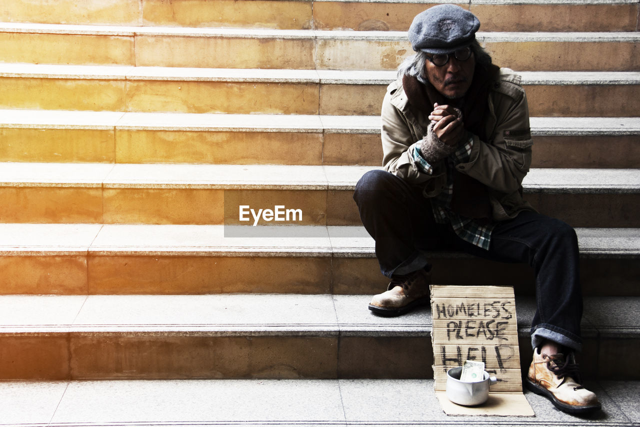 Beggar with text on cardboard sitting on steps