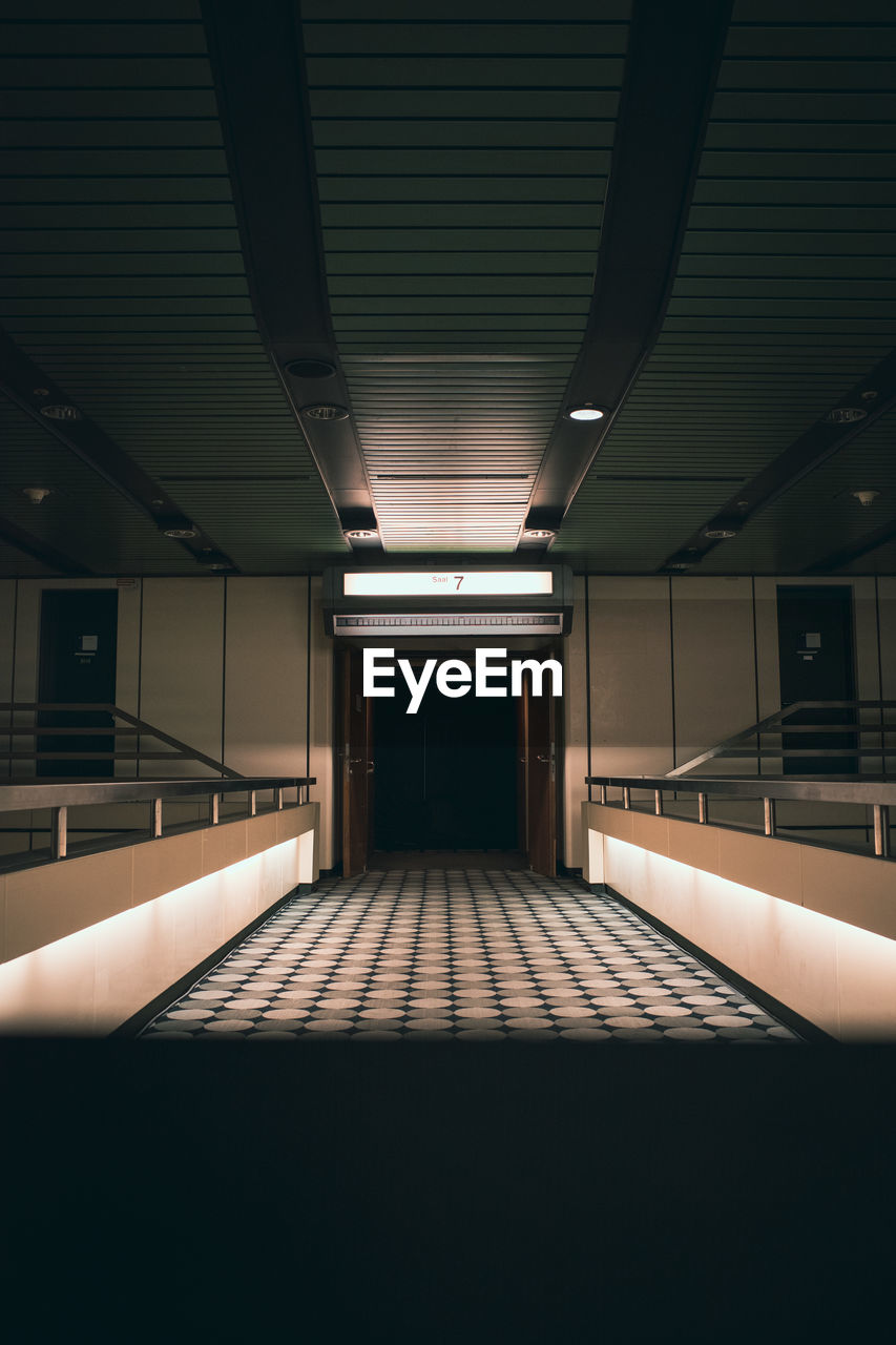 EMPTY CORRIDOR ALONG ILLUMINATED BUILDING