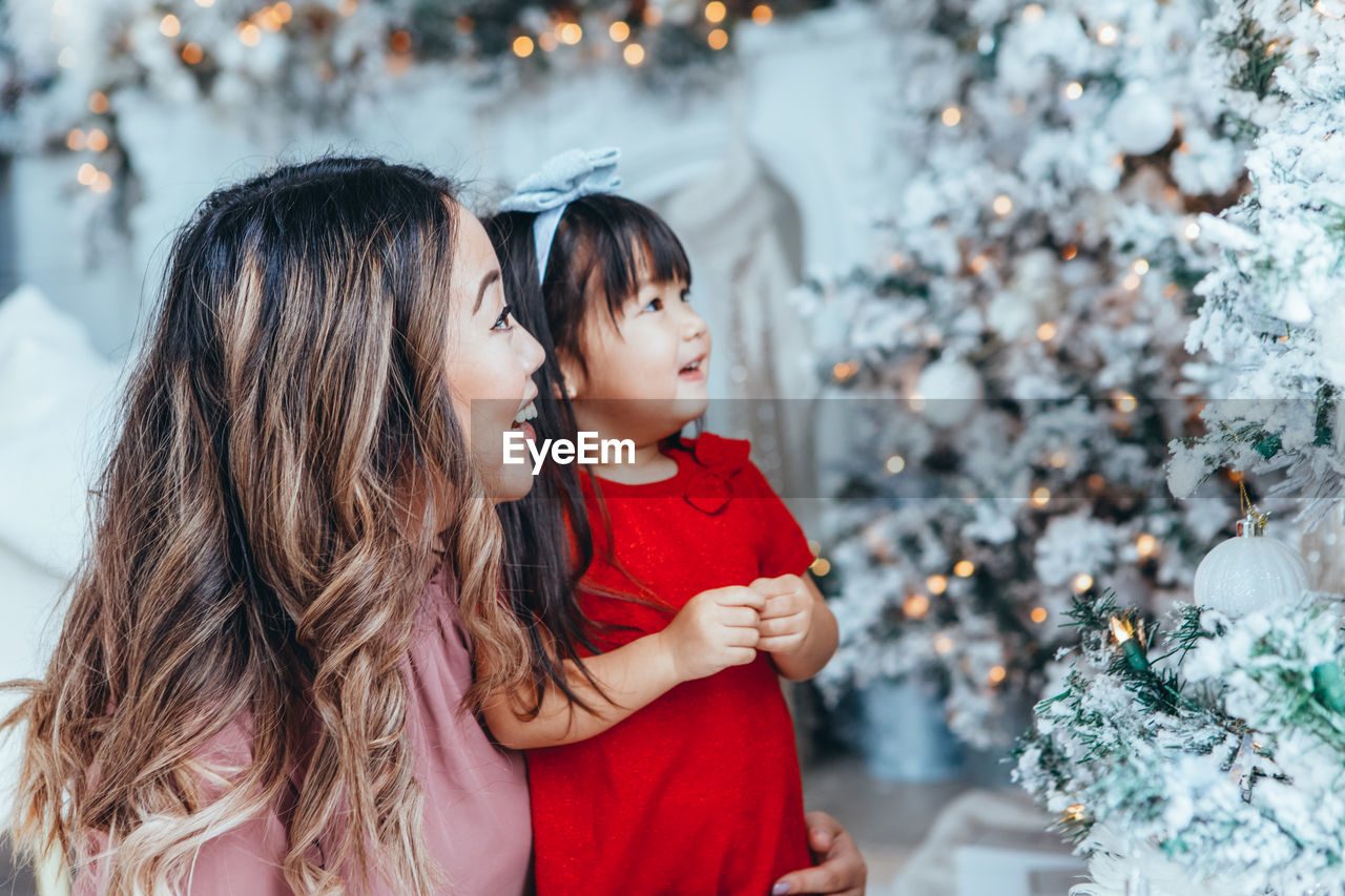 Happy mother and daughter touching christmas tree at home