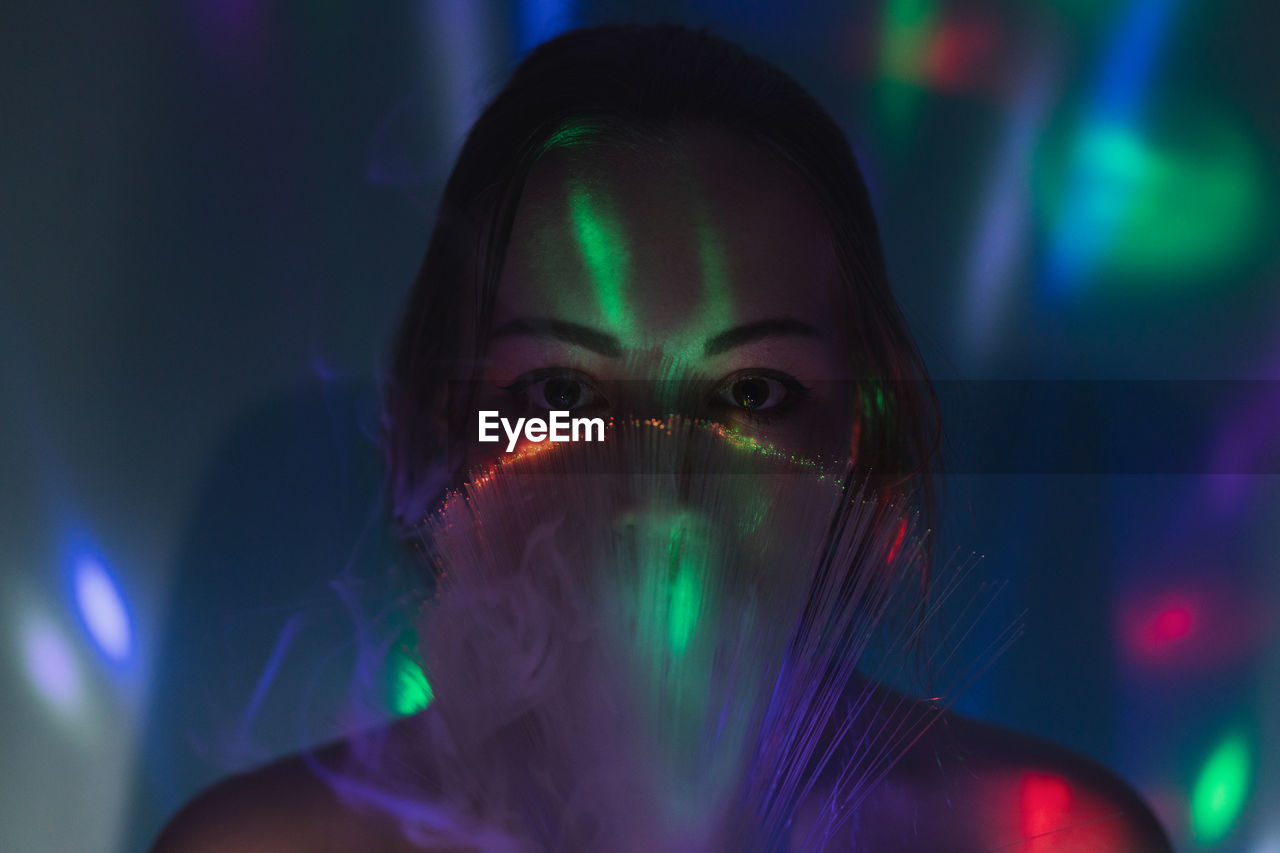 Close-up portrait of young woman holding multi colored fiber optic and smoke