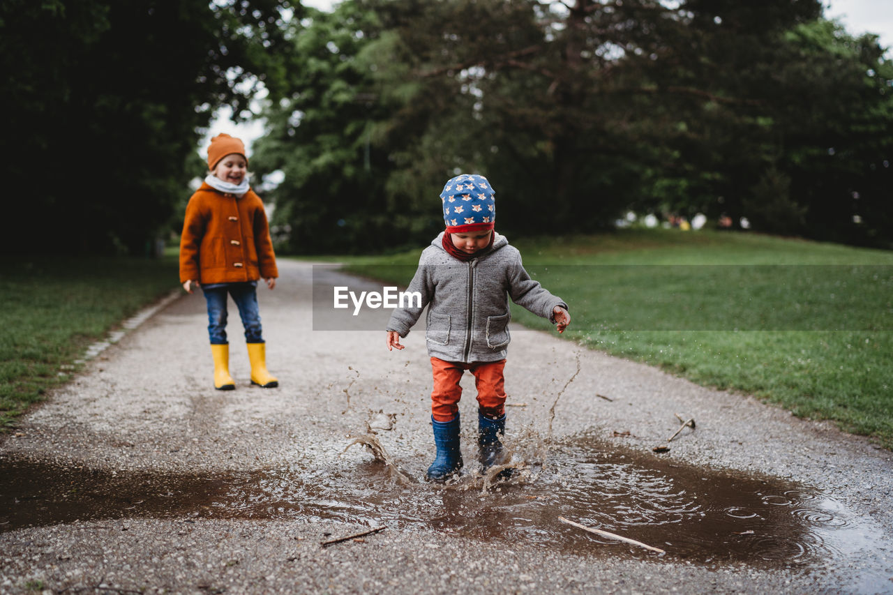 Young boys jumping in the puddles at the park on cloudy day