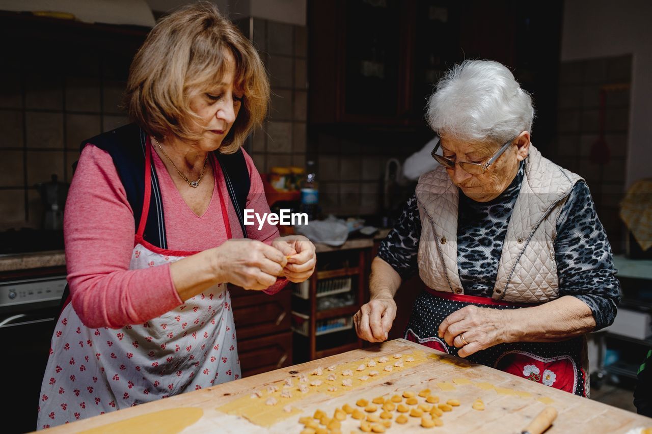 Busy senior women standing at table and preparing traditional domestic tortellini for dinner at home