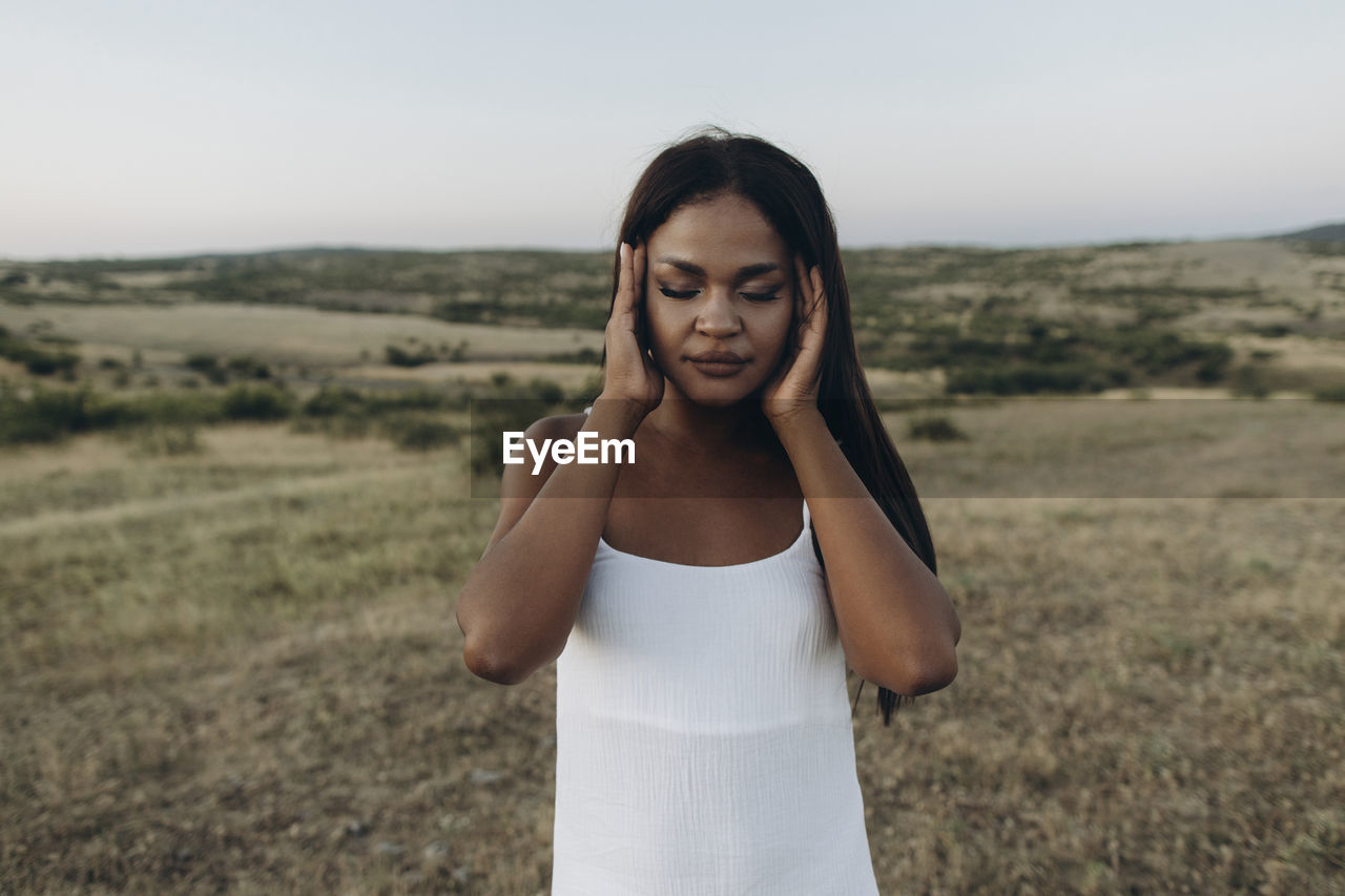 Woman with eyes closed rubbing head in meadow