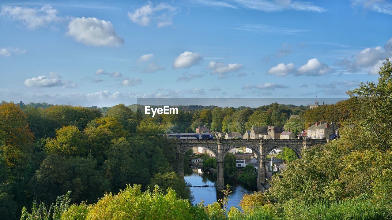 BRIDGE OVER RIVER AMIDST TREES AGAINST SKY