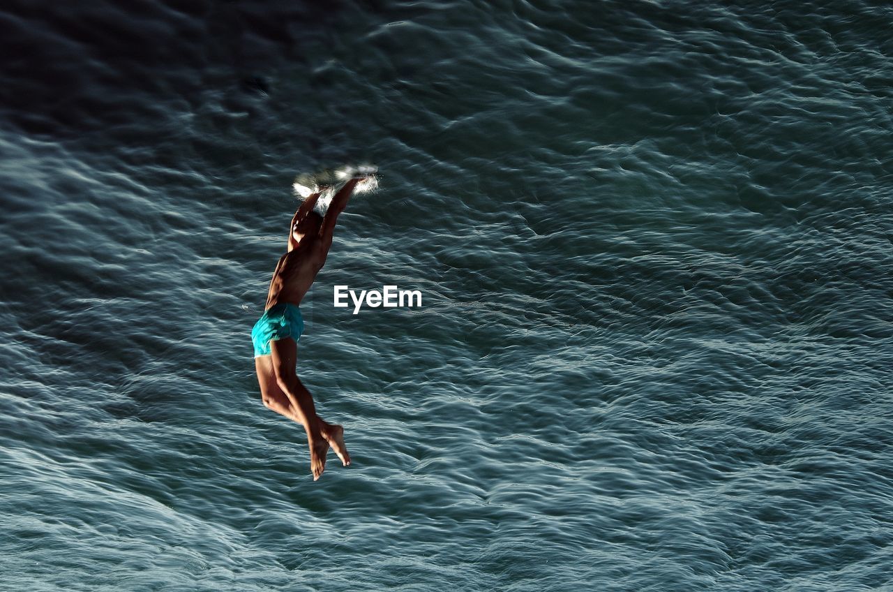 Upside down image of shirtless man diving into sea