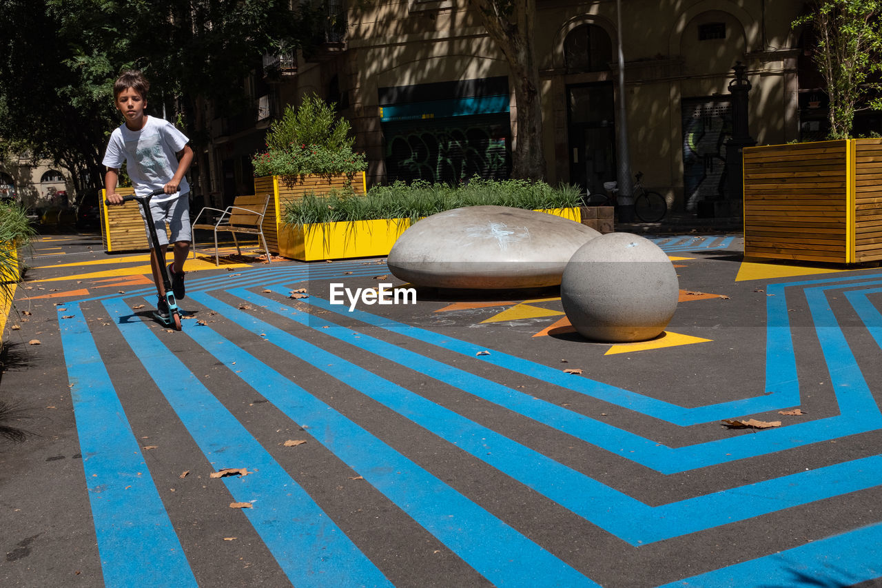 A child rides a scooter in a public space with street furniture located in barcelona, spain.