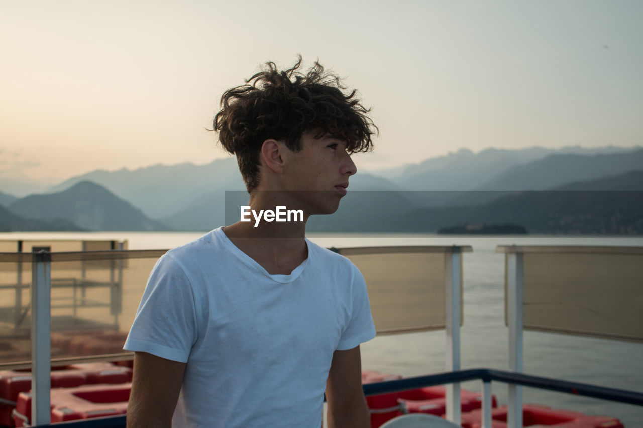 Young man standing on pier against sky during sunset