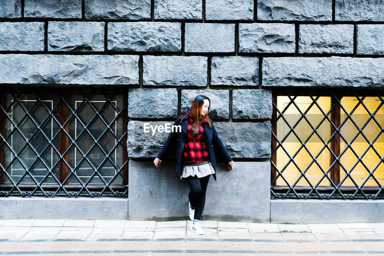 Full length of woman standing against stone wall