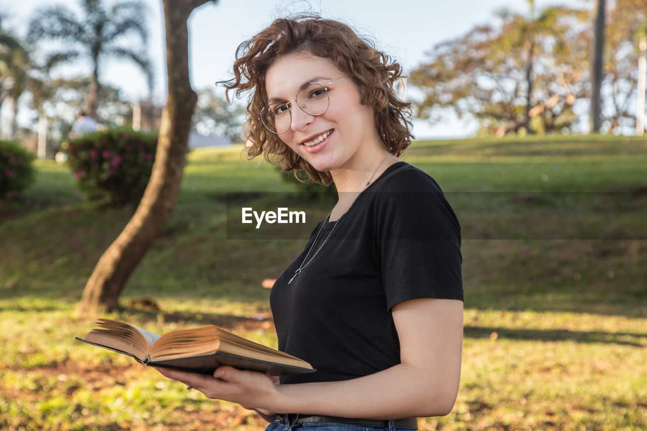 Portrait of smiling young woman reading book on field