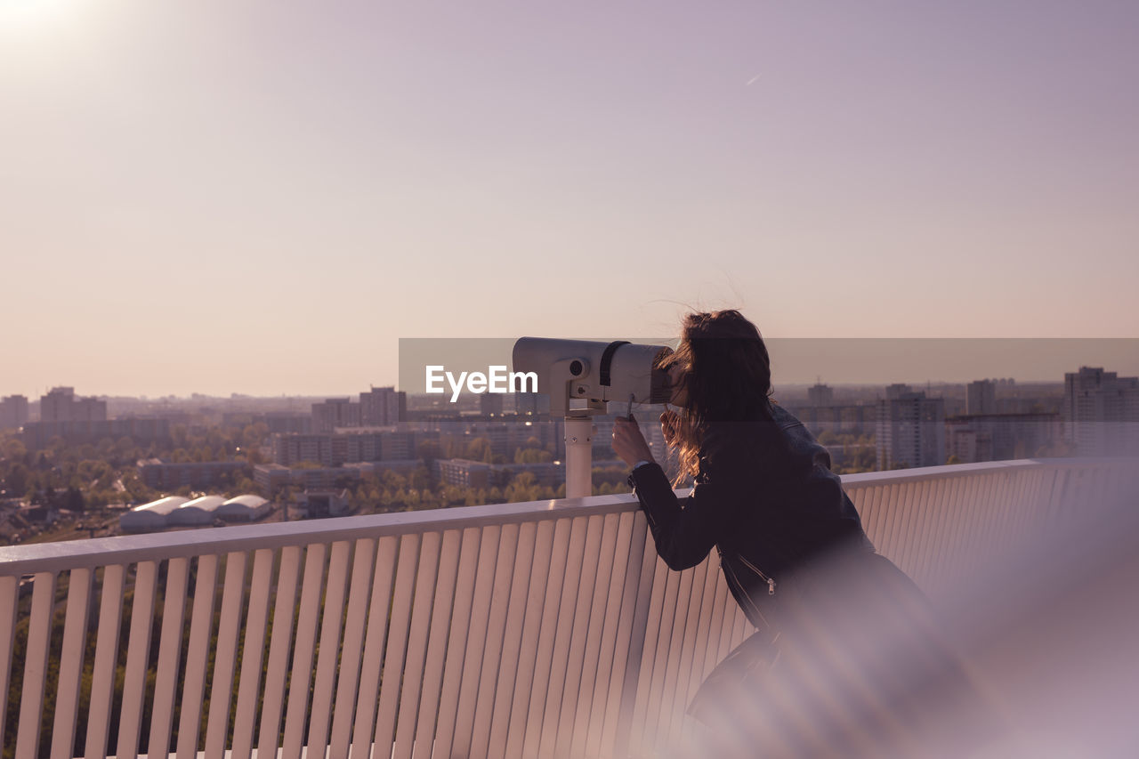 Side view of woman looking through coin-operated binoculars while standing on observation point