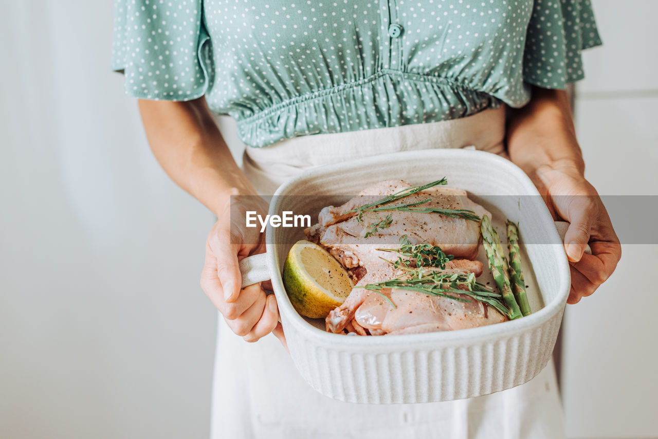 Close up hands holding a tray with raw quail and aromatic herbs