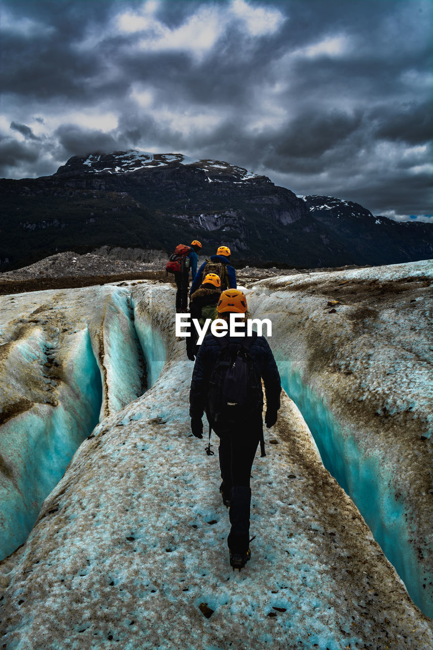 Rear view of hikers walking on rock against cloudy sky