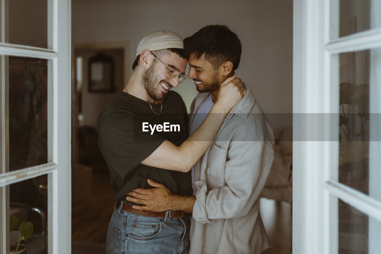 Loving gay couple standing with each other smiling at home