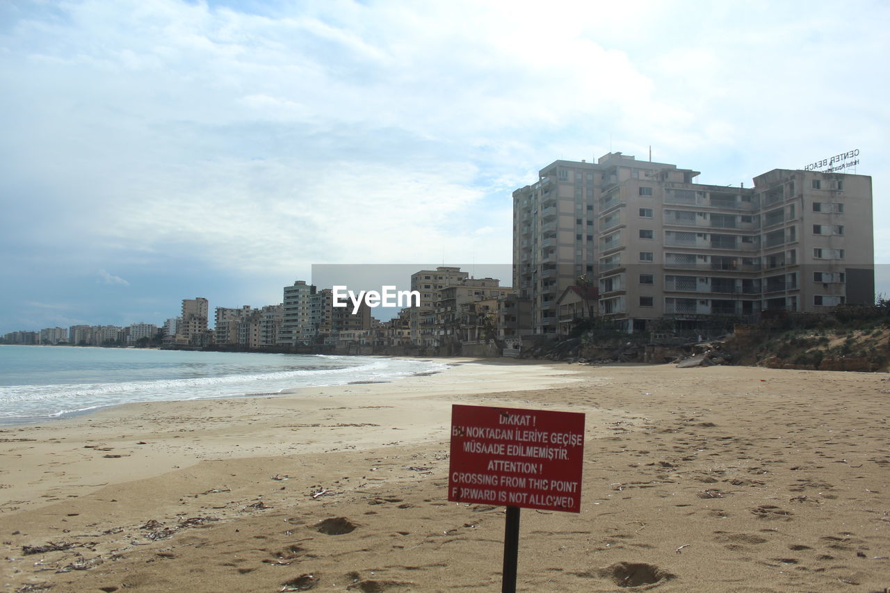 beach, sky, land, architecture, sand, sea, built structure, water, communication, coast, city, building exterior, text, nature, sign, cloud, building, western script, shore, body of water, urban skyline, travel destinations, no people, ocean, day, outdoors, office building exterior, landscape, coastline, skyscraper, warning sign, travel, vacation, horizon