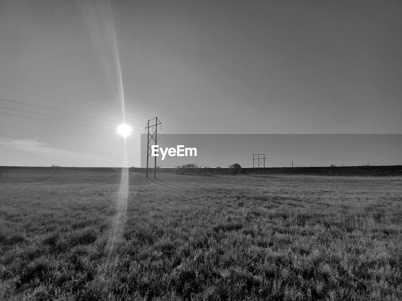 ELECTRICITY PYLONS ON FIELD AGAINST SKY