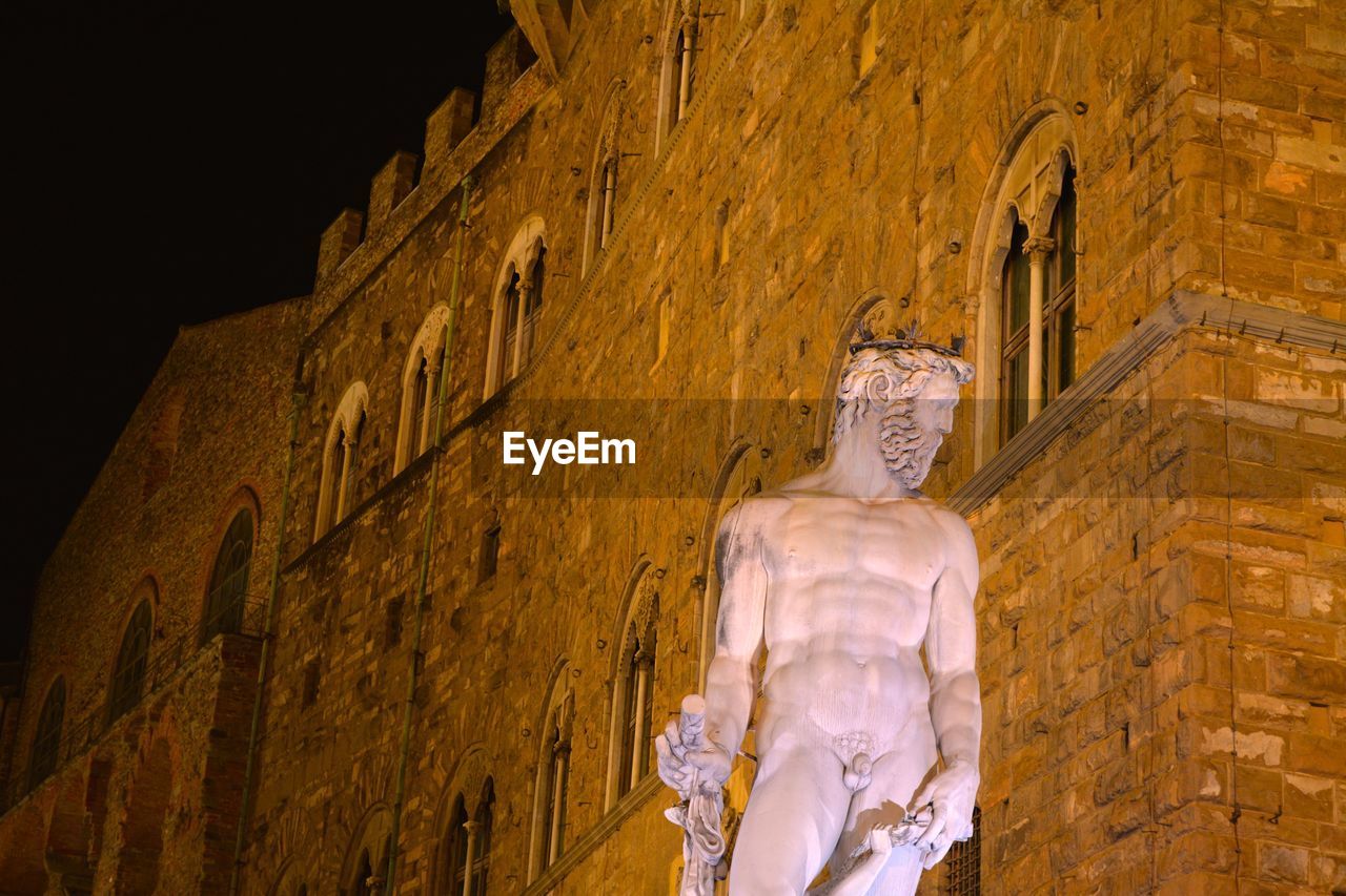 Low angle view of statue against building in city at night