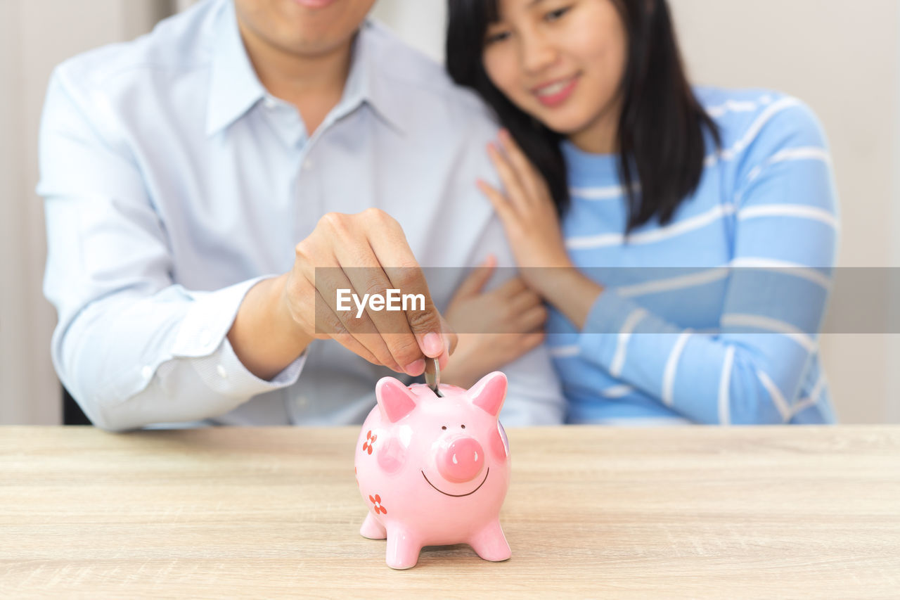 Midsection of man sitting by woman while inserting coin in piggy bank