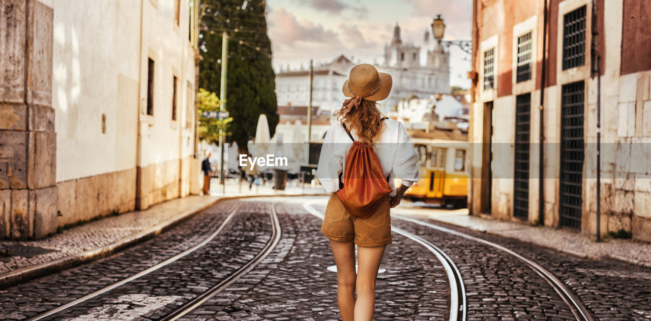 Rear view of woman walking on railroad tracks in city