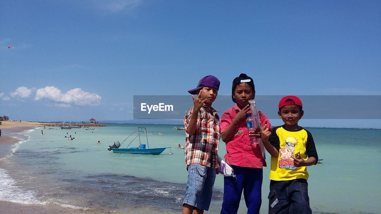 FRIENDS STANDING AT BEACH DURING SUNNY DAY