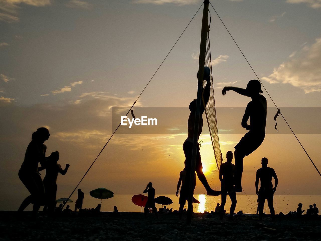 Silhouette friends playing volleyball at beach against sky during sunset