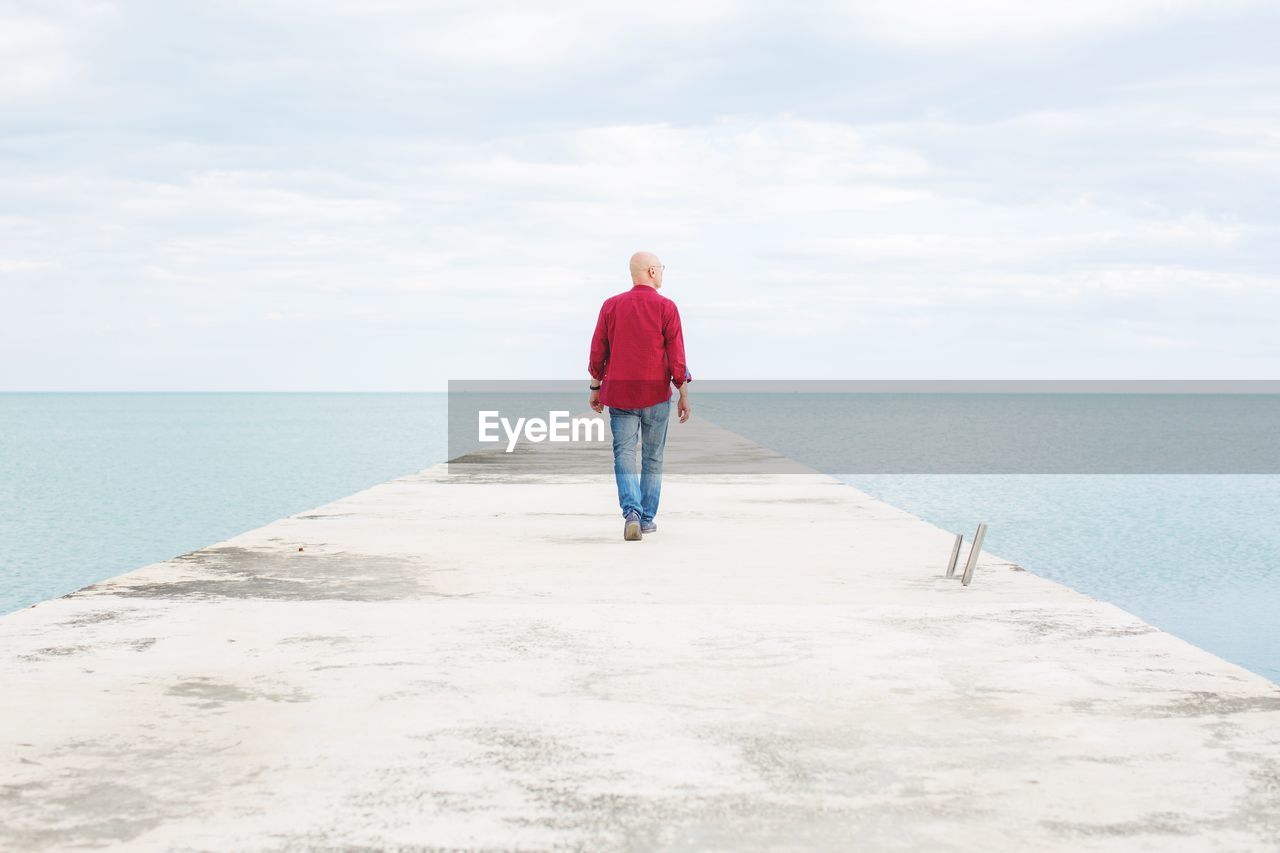 Rear view full length of man walking on pier amidst sea against sky
