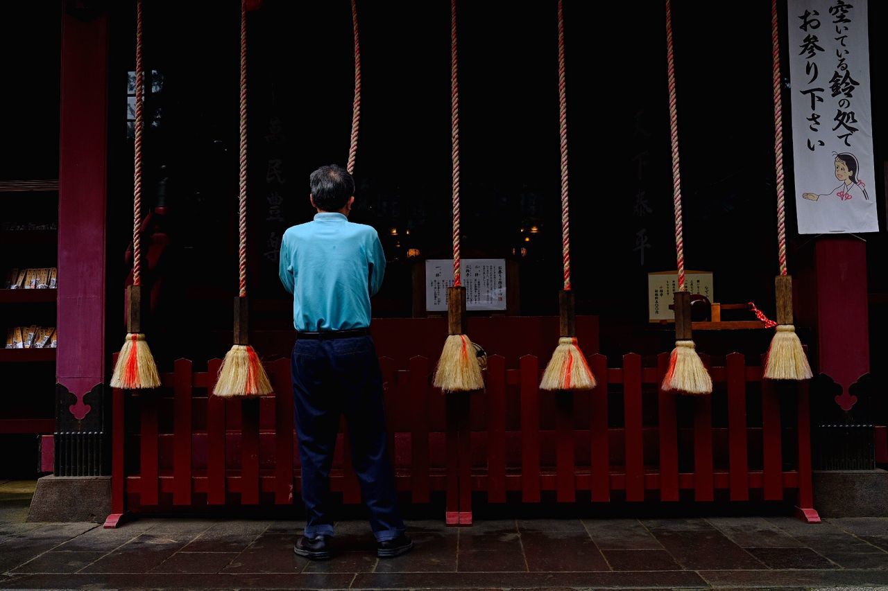 Rear view of man praying while standing by huge tassels at japanese temple