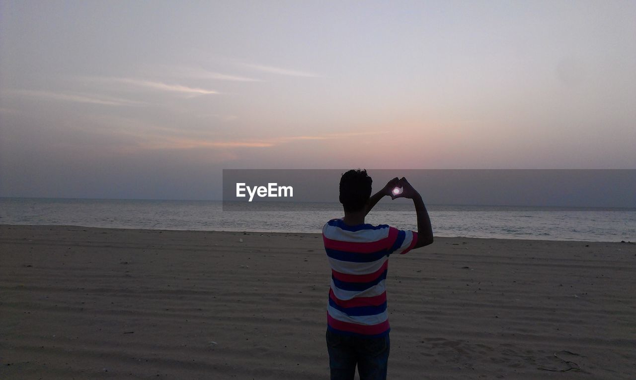 REAR VIEW OF WOMAN STANDING ON BEACH