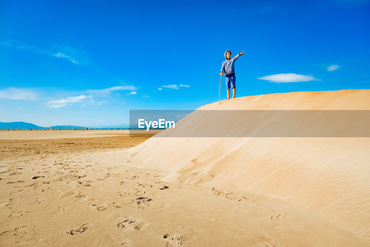 rear view of man walking on sand at beach against blue sky