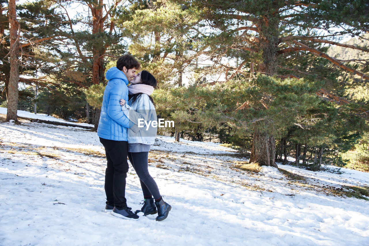 Full length side view of young couple falling in love while standing on snow