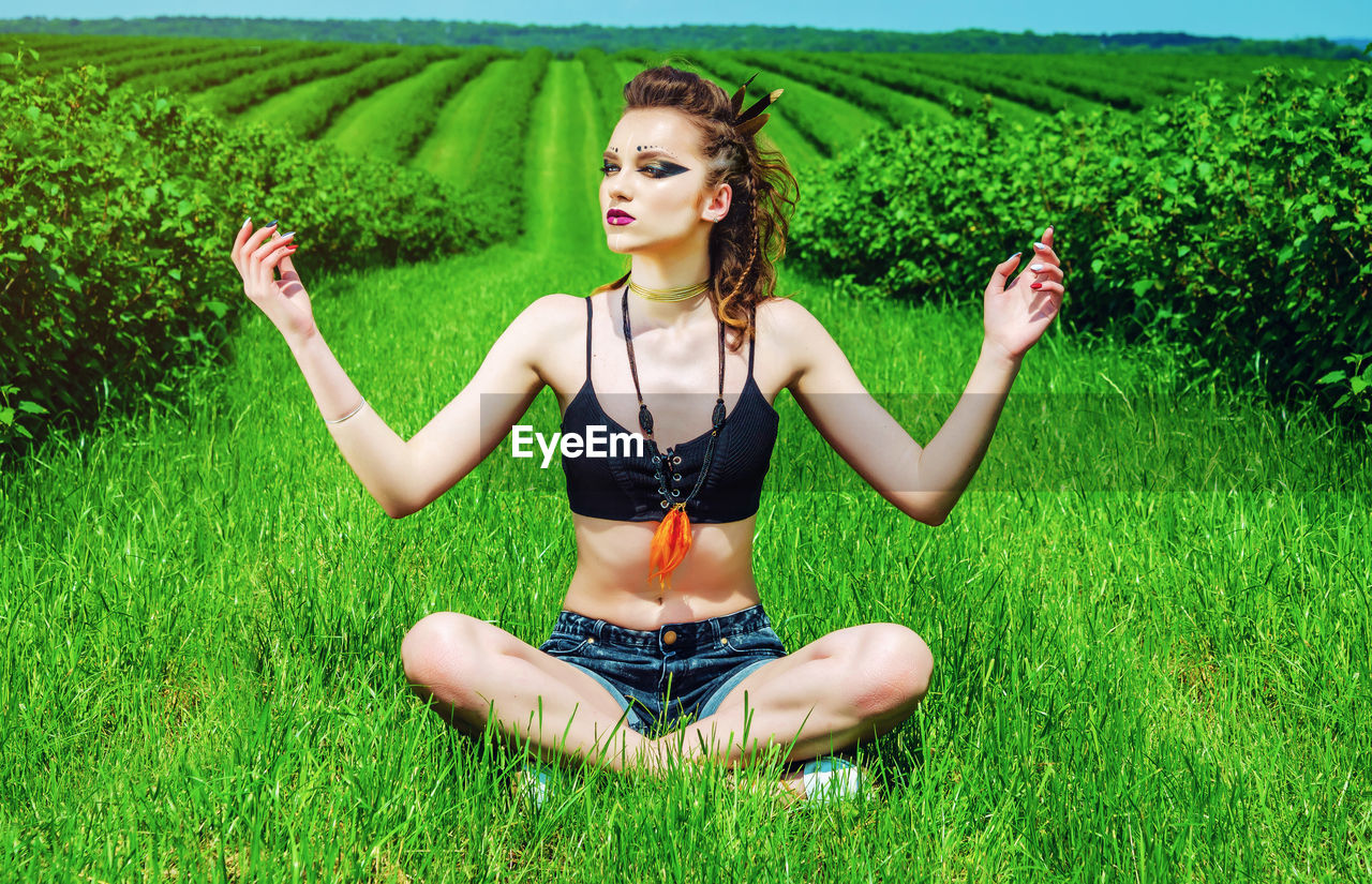 Young woman with arms raised sitting on field