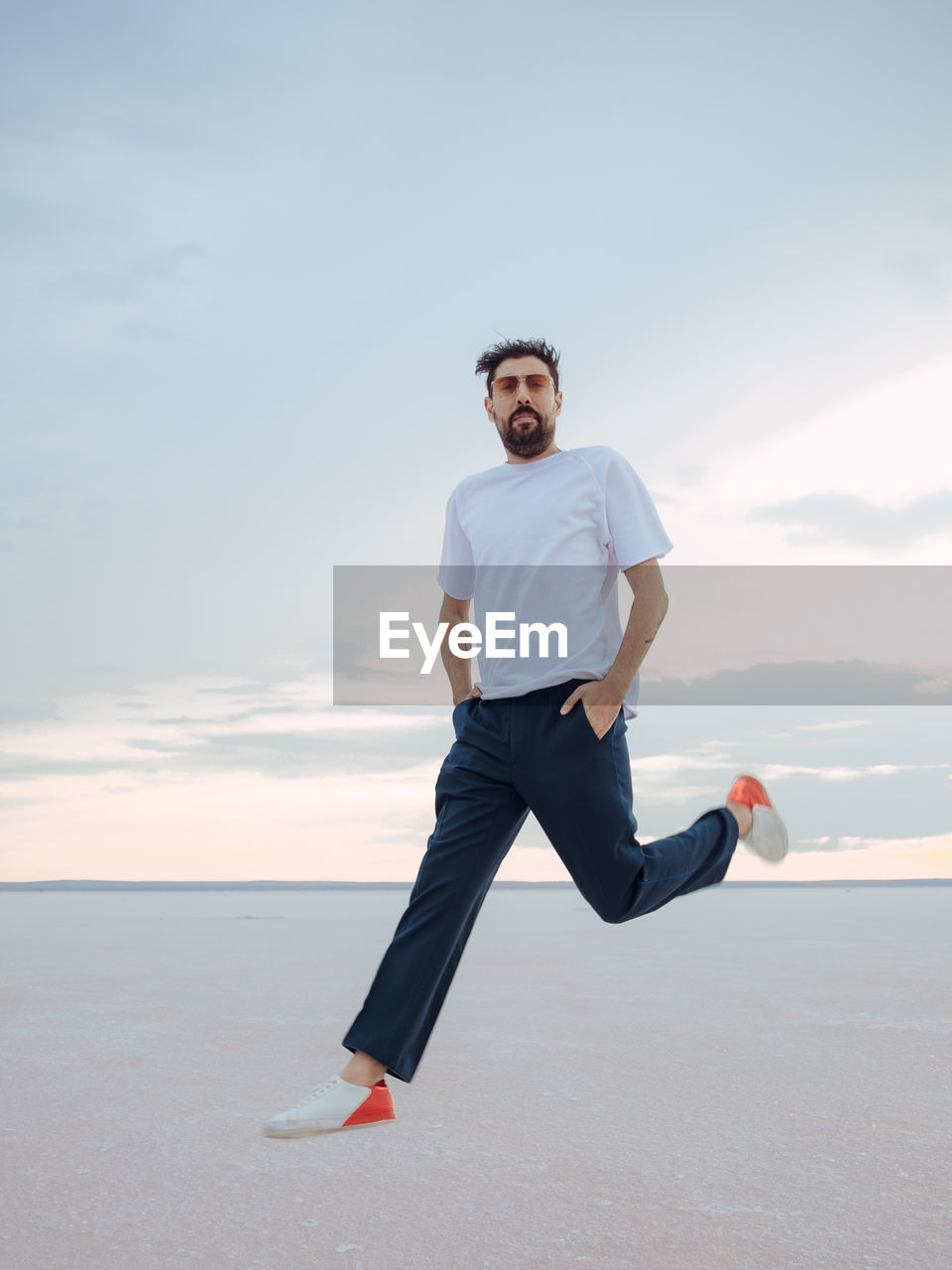 Portrait of young man running on sand at beach against sky