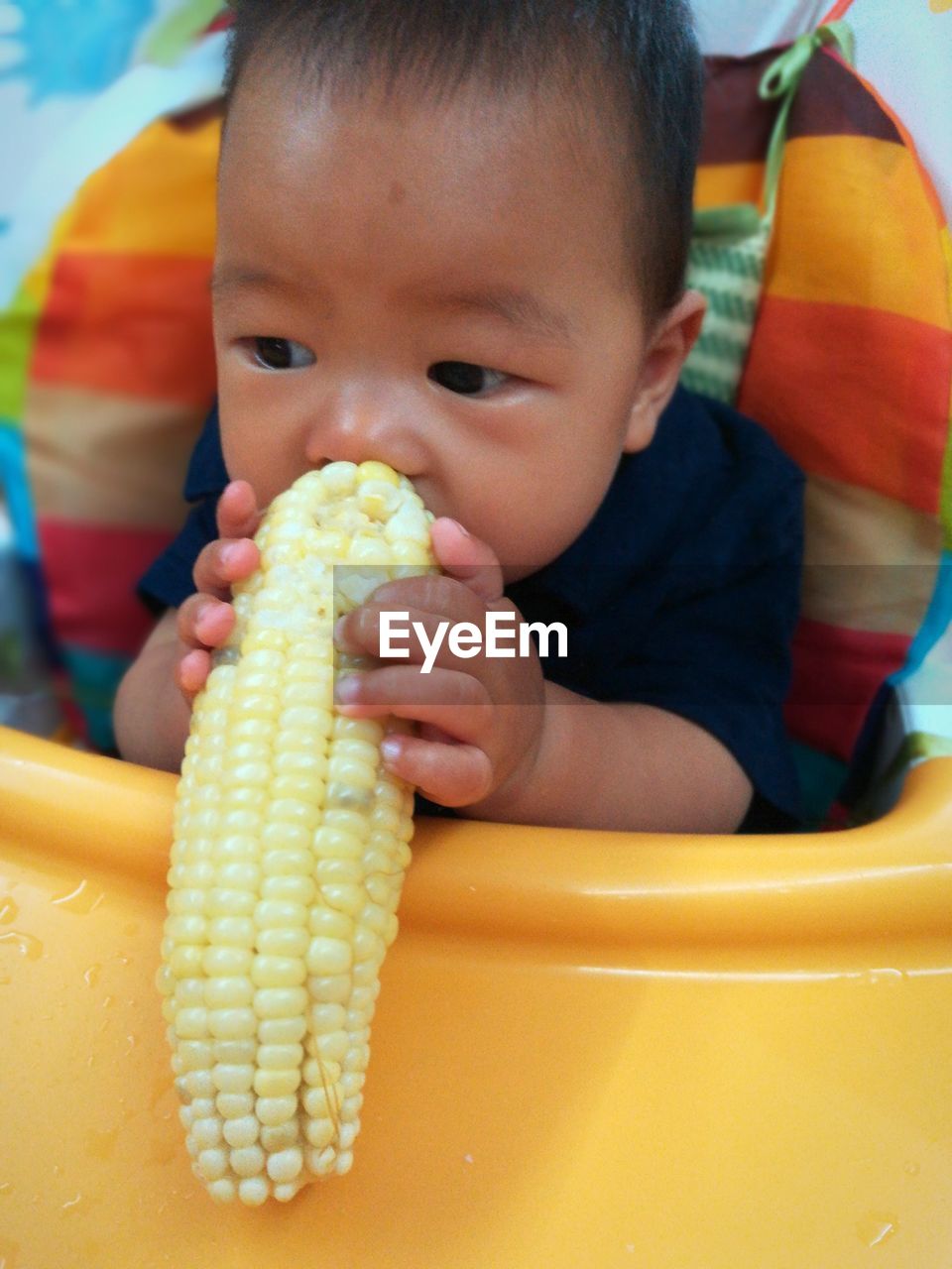 Close-up of baby boy eating sweetcorn while sitting on chair