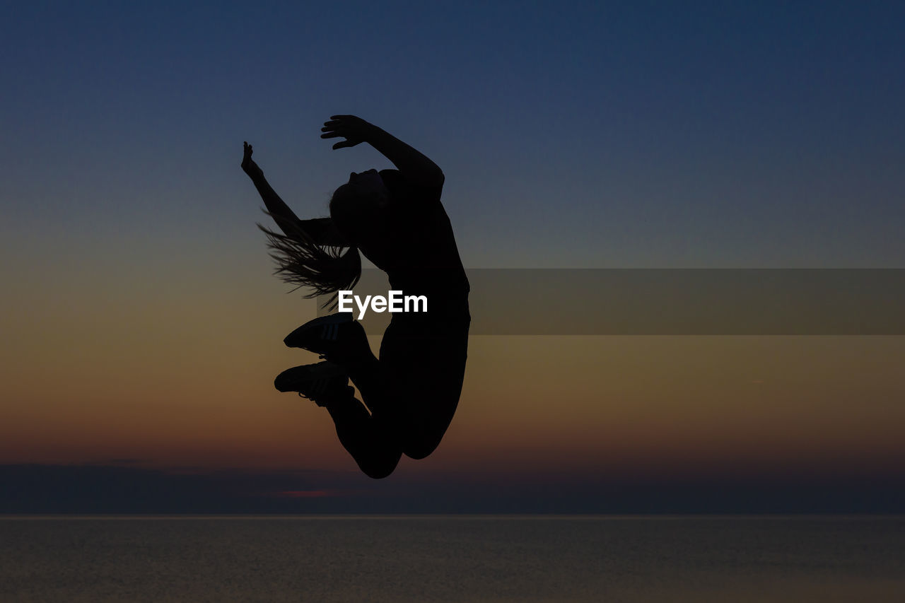 Silhouette woman jumping over sea against sky during sunset