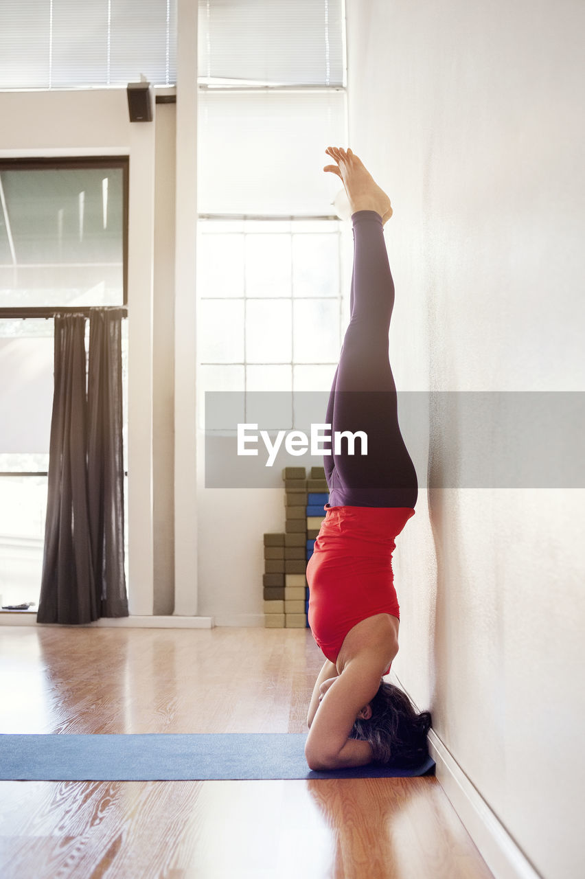 Side view of woman performing headstand at health club