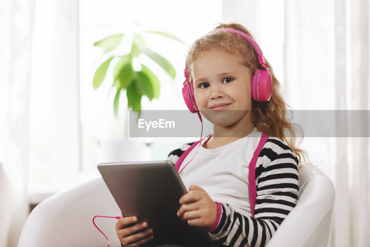 A school girl in pink headphones sits with a tablet and listens to an online lesson.online education