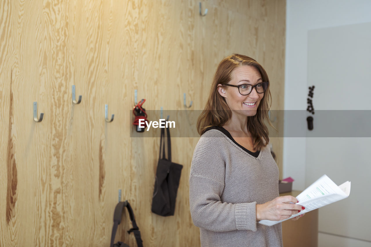 Smiling confident businesswoman holding documents while standing at office