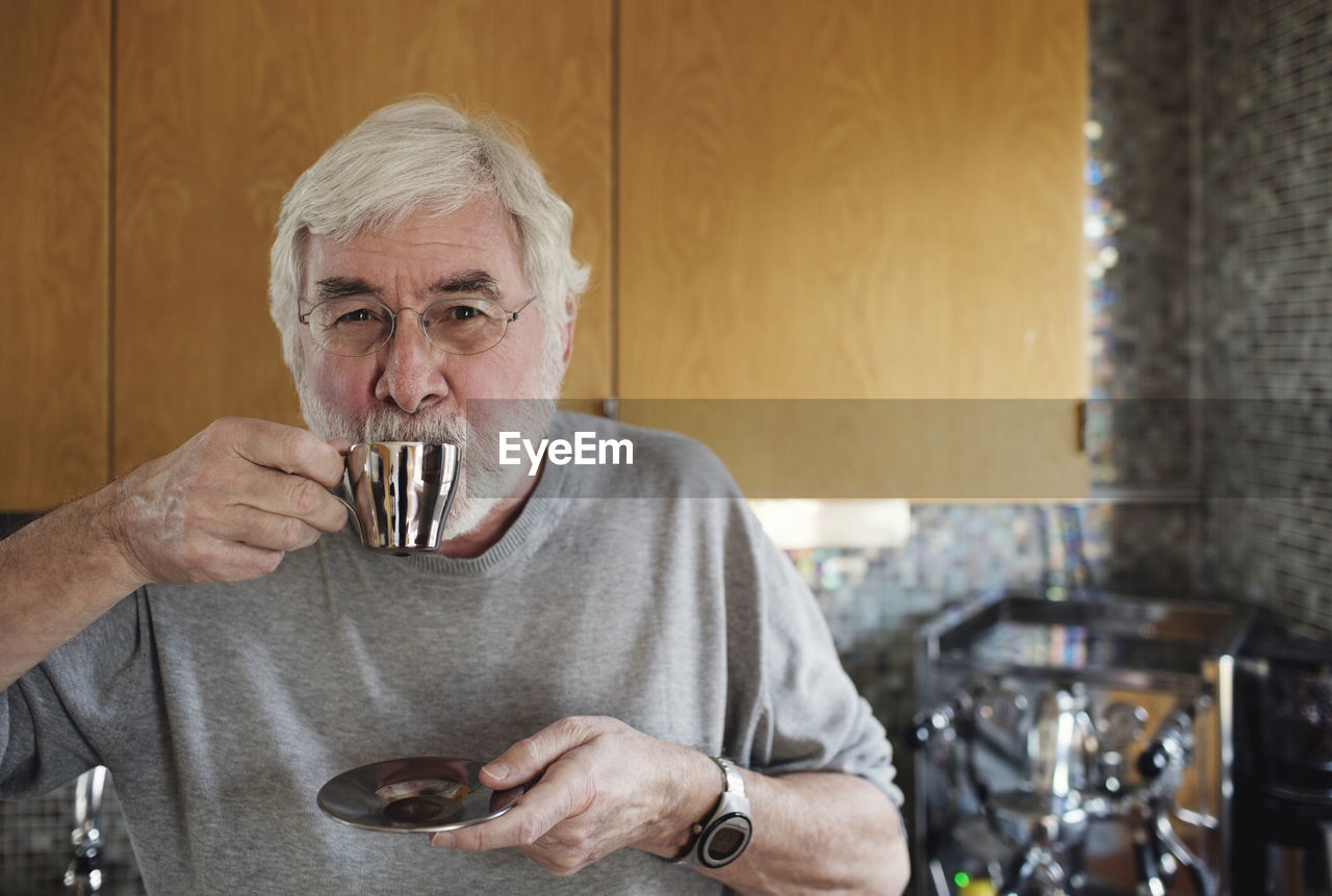 Portrait of senior man drinking coffee while standing in kitchen
