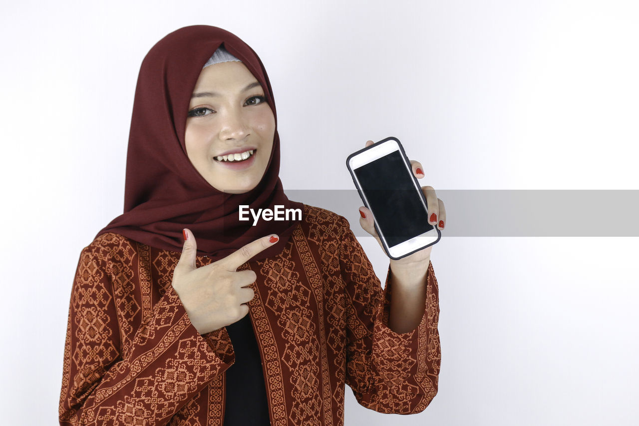 PORTRAIT OF YOUNG WOMAN USING PHONE AGAINST WHITE BACKGROUND